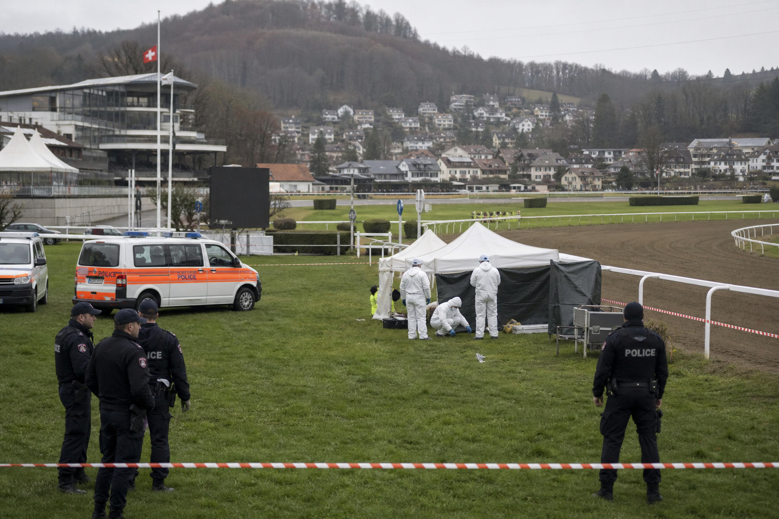 Police officers and forensic investigators behind cordon tape near the Schachen racetrack in Aarau in daylight