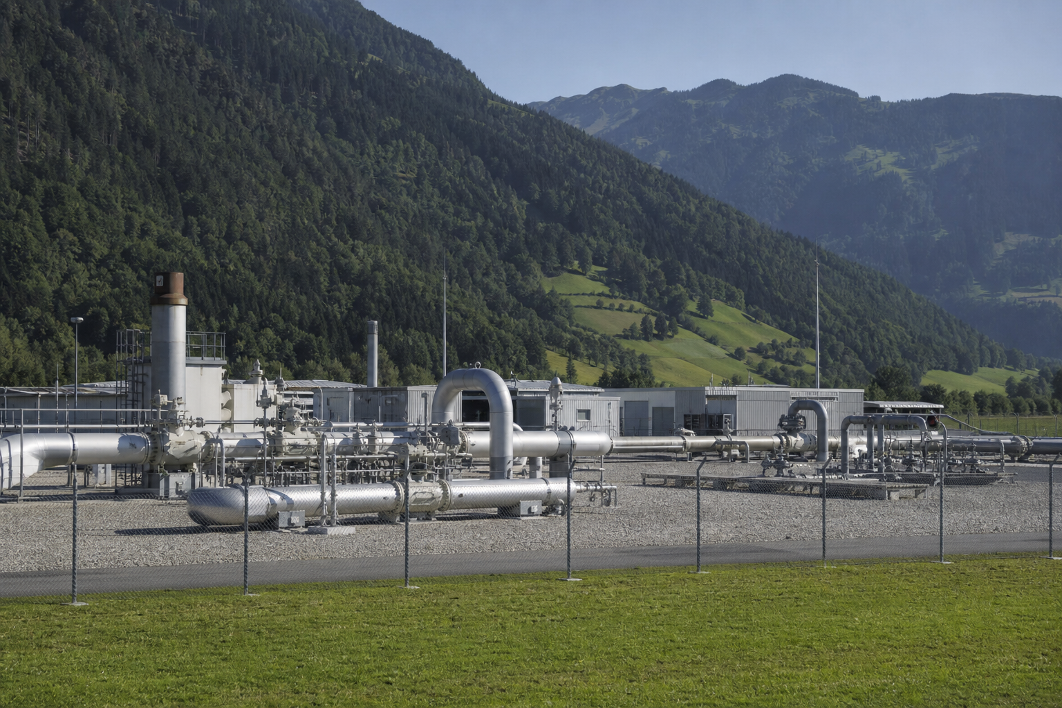 Gas pipeline infrastructure and a compressor station in a Swiss valley with mountains beyond