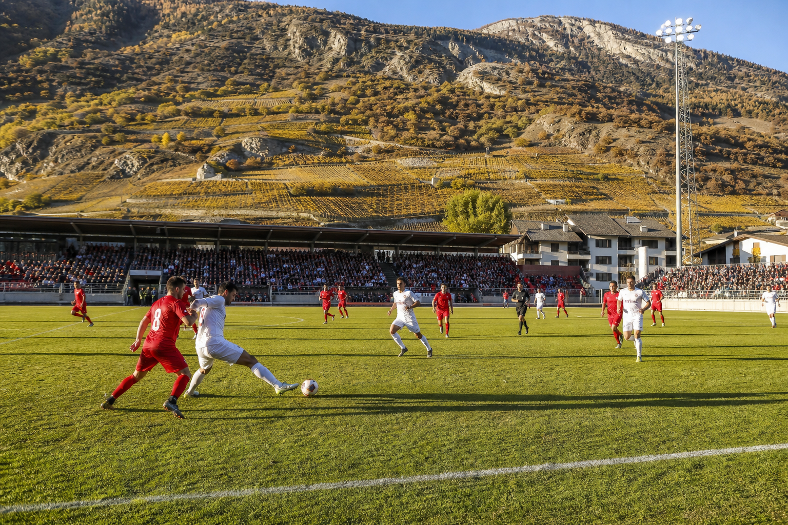 A football match in a Valais stadium with steep alpine slopes behind the stands